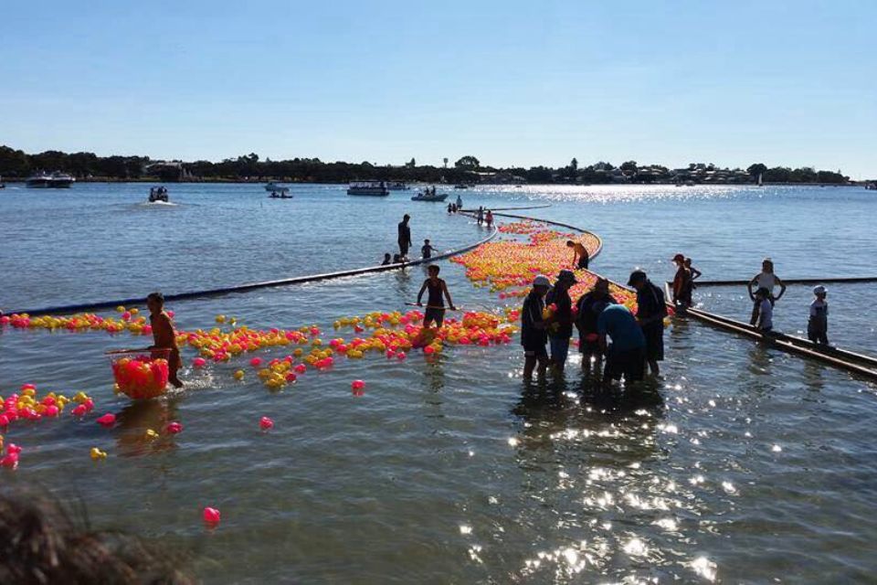 a group of people standing in the water with orange and yellow plastic ducks