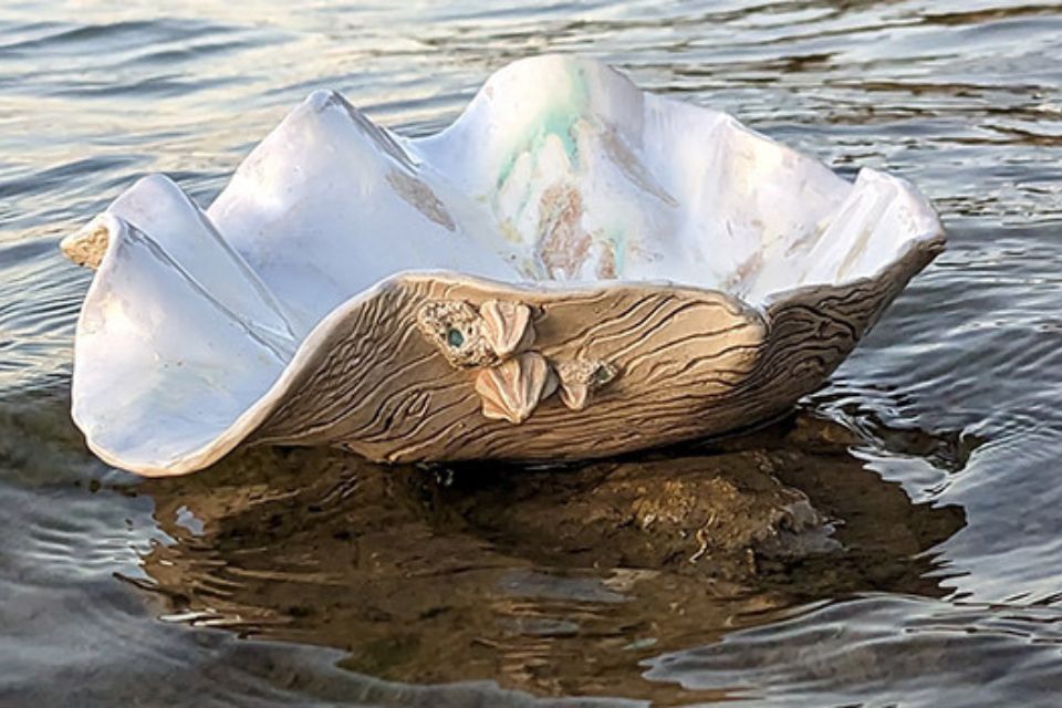 a shell bowl made of clay sitting on top of water in the middle of a body of water