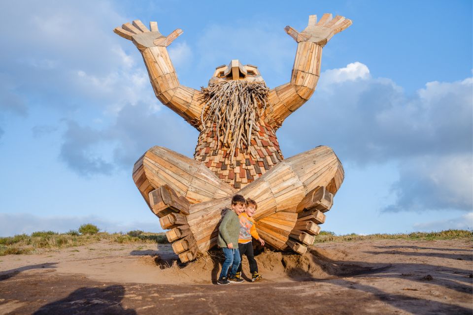 two children standing in front of a giant wooden sculpture