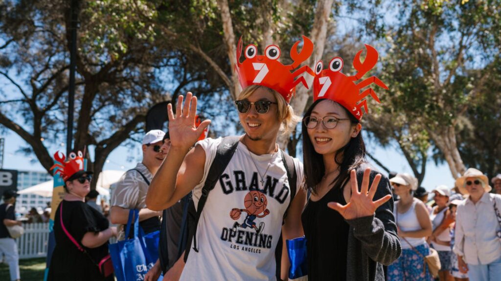 two Asian tourists wearing crab hats at Crab Fest Mandurah and waving at the camera