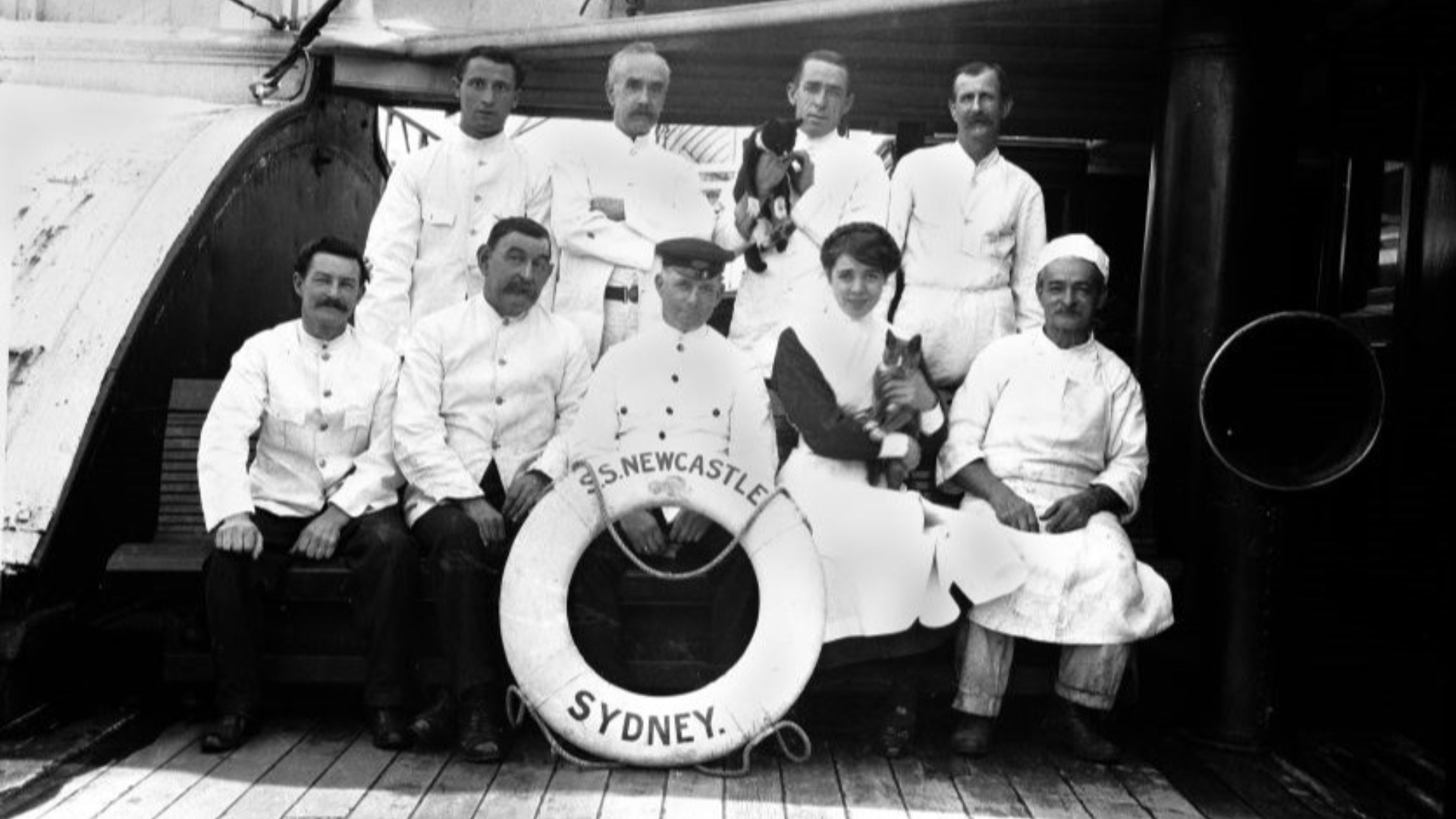 A historical photo of a group of people sitting on the deck of a ship