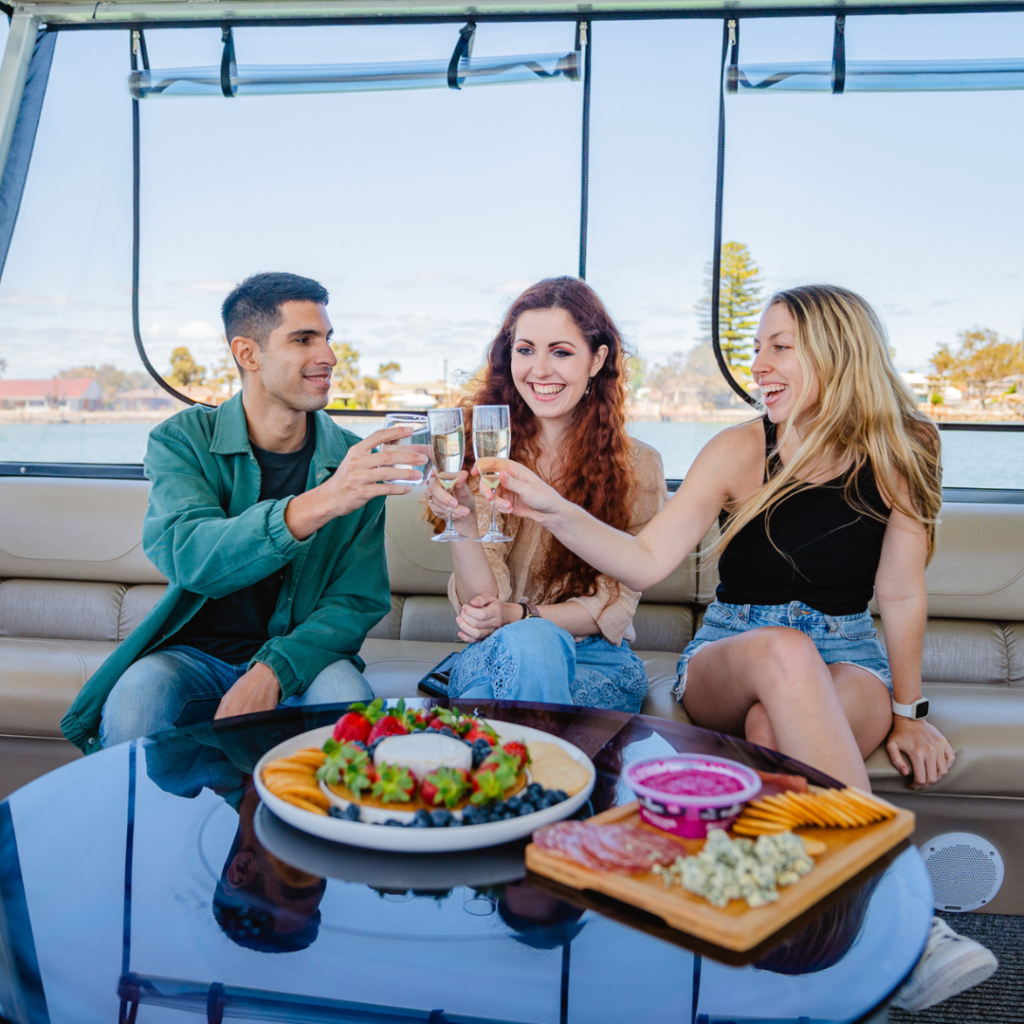 a young men and two young women toasting on a comfortable charter boat with food and drinks