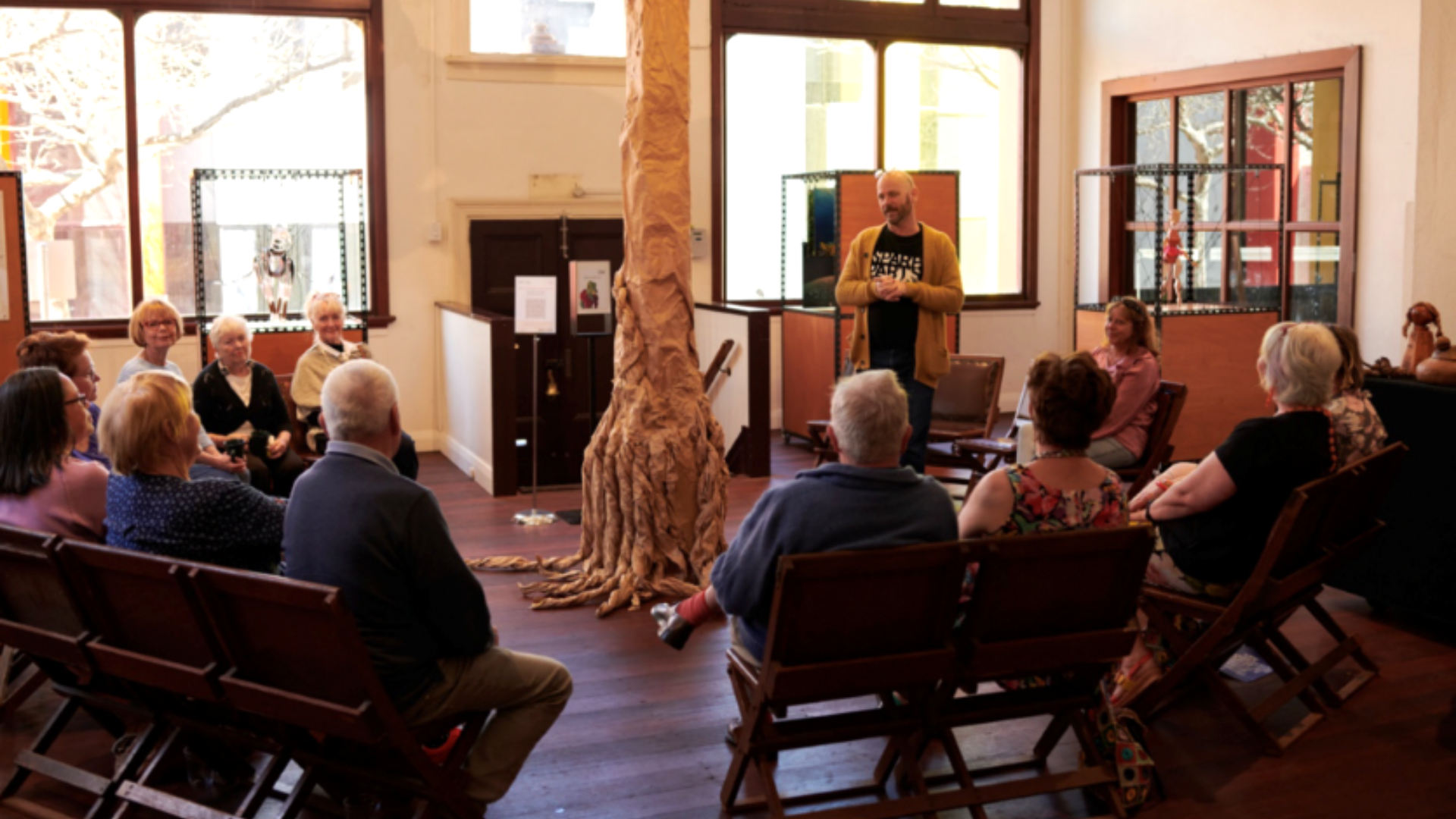 a group of old people sitting in chairs inside a building where there is a tree in the centre