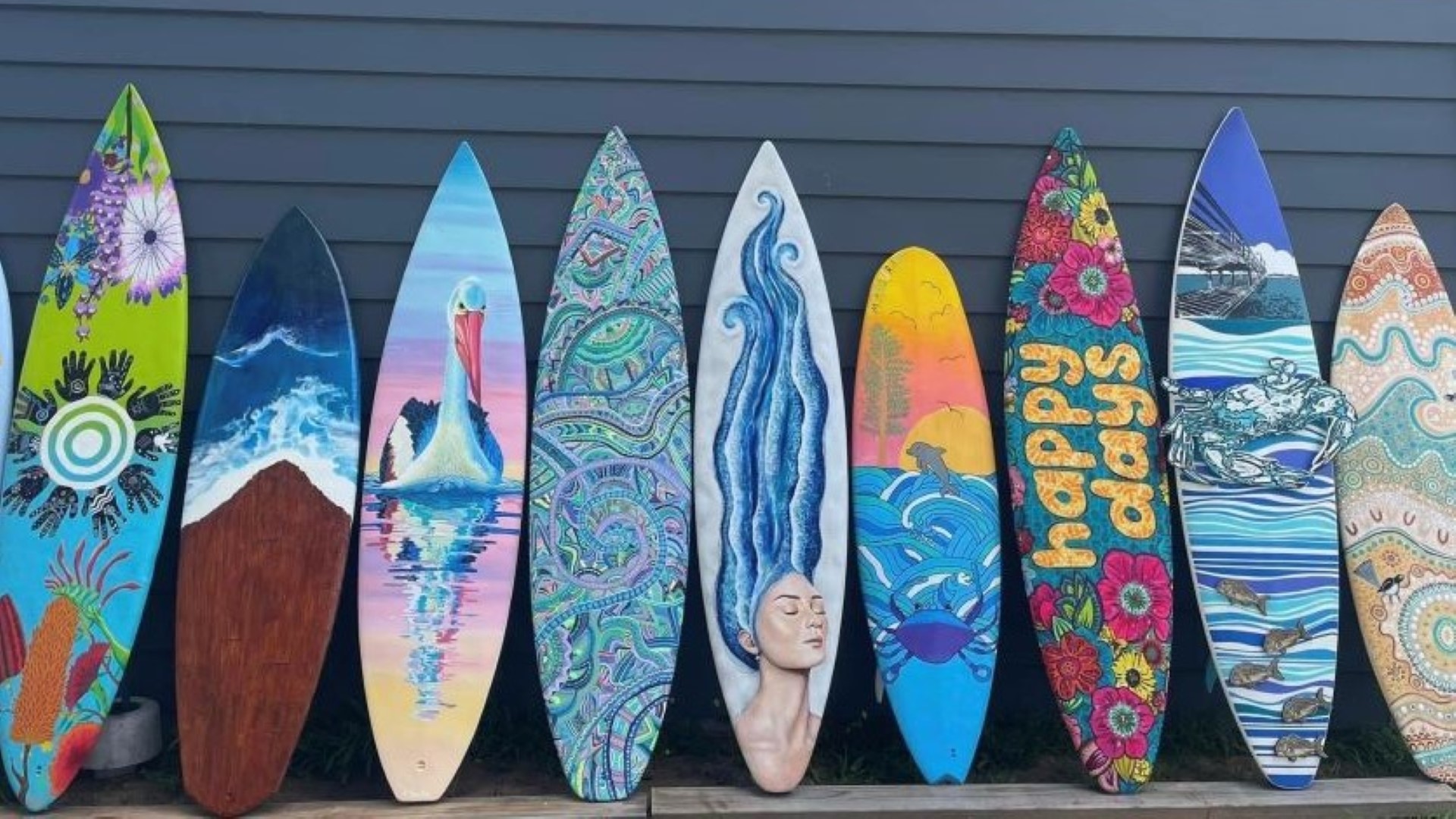 Several colourful surfboards lined-up in a row leaning against a wall