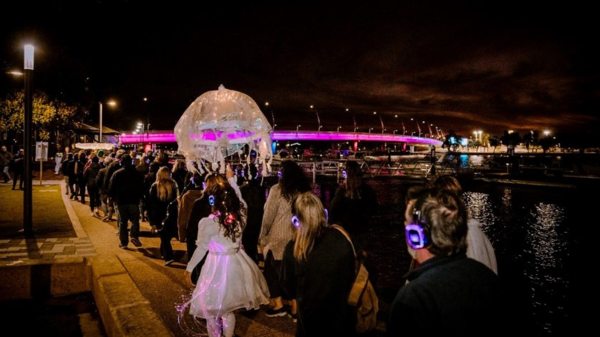 a crowd of people walking along the waterfront at night