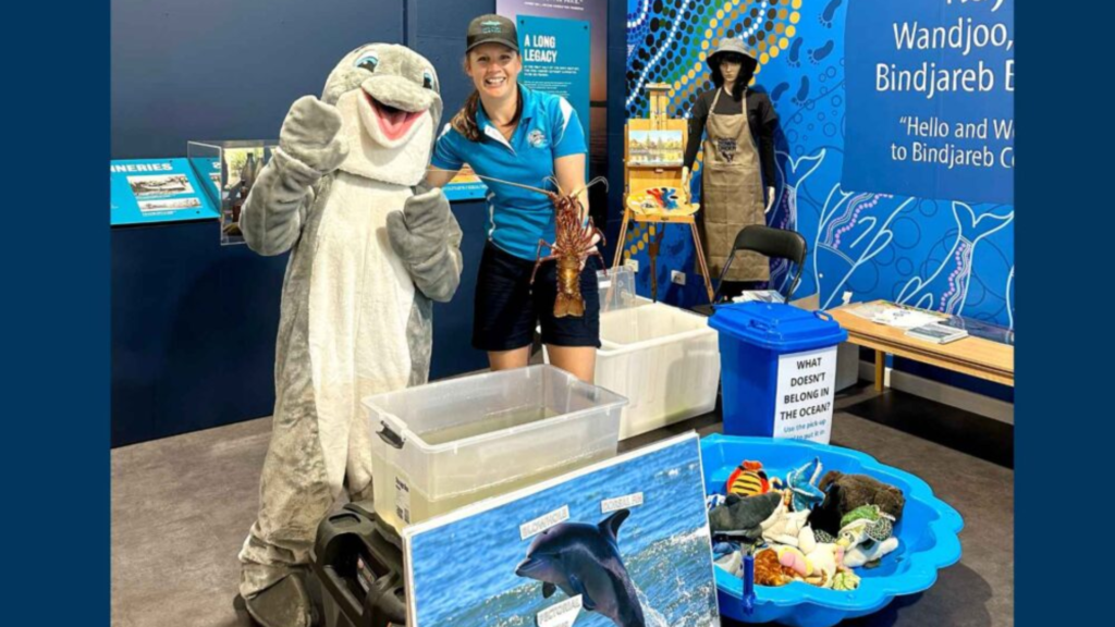 a young woman in a blue shirt standing next to a person in a dolphin costume