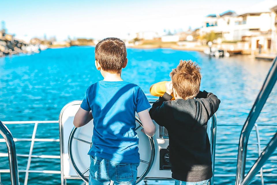 Two young boys standing on the deck of a boat looking out at the water