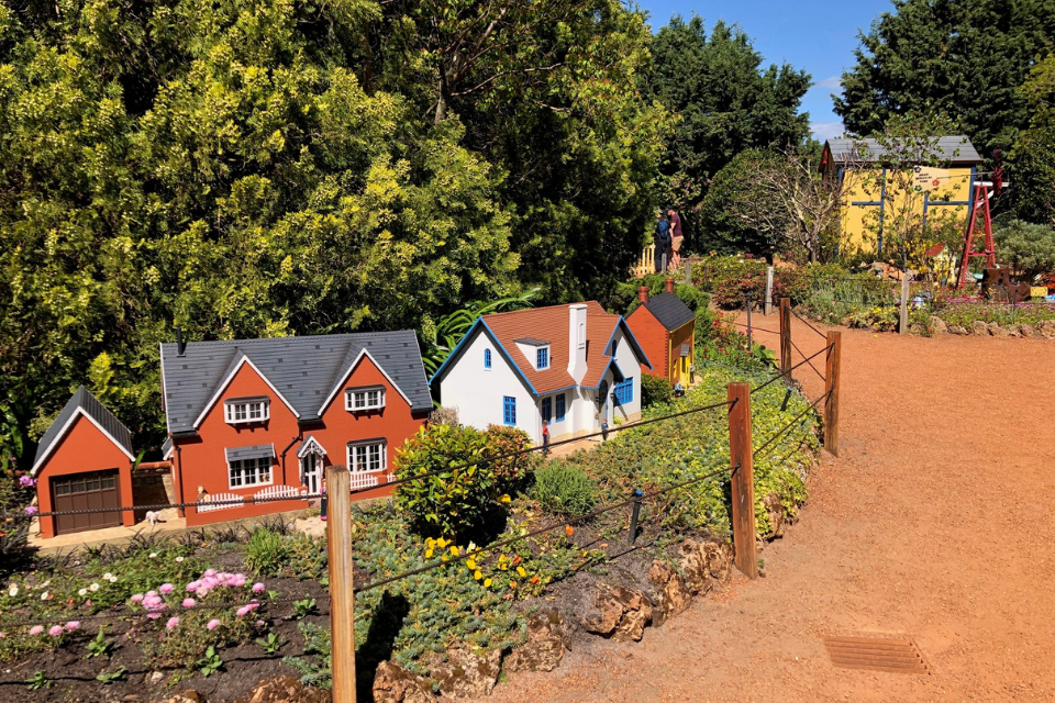 a miniature village with houses and trees on the side of a gravel path