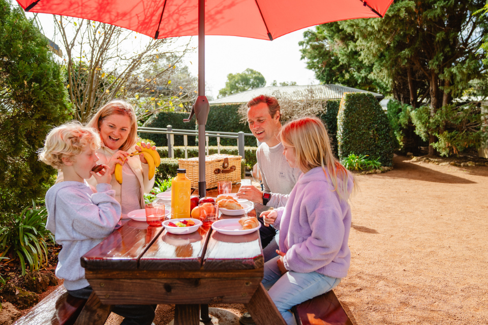 a family sitting at a picnic table under a red umbrella