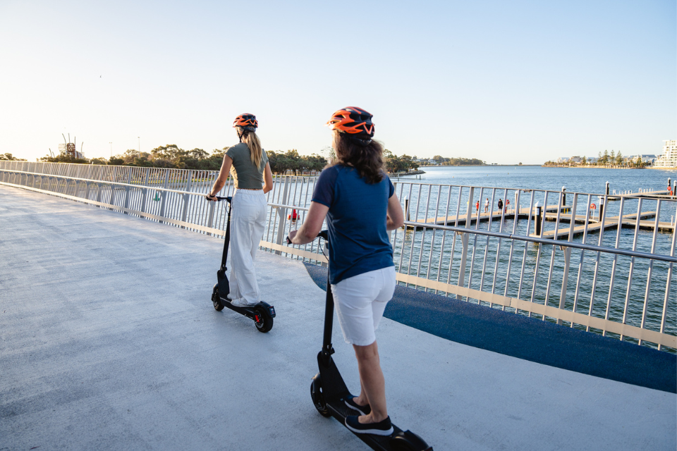 two women riding electric scooters across the Mandurah Bridge