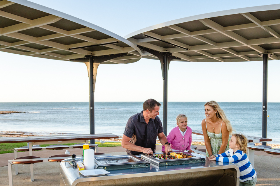 a family is cooking on an outdoor grill at the beach