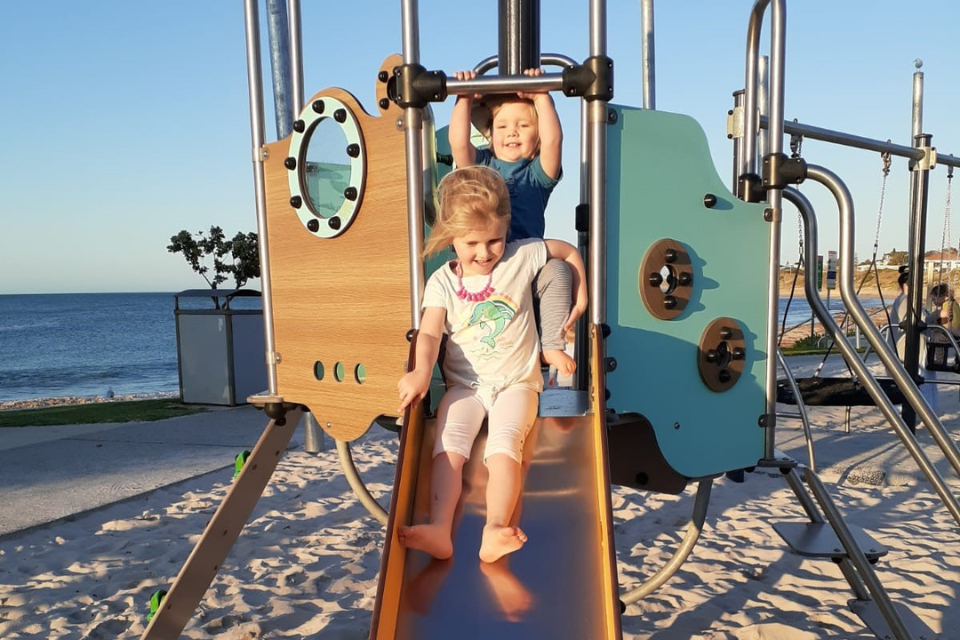 two children on a playground slide at the beach