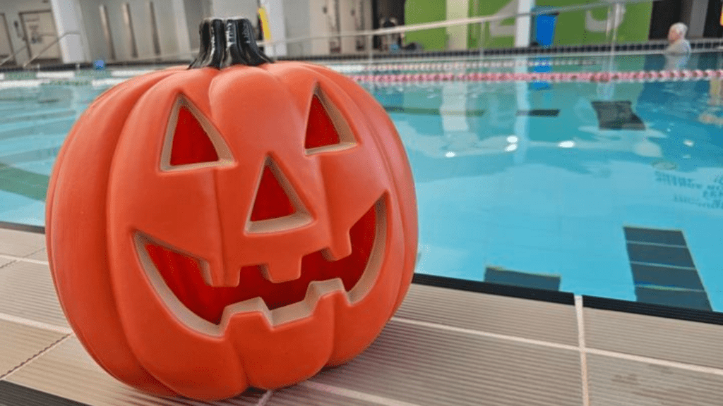 a halloween pumpkin sitting on the edge of a swimming pool