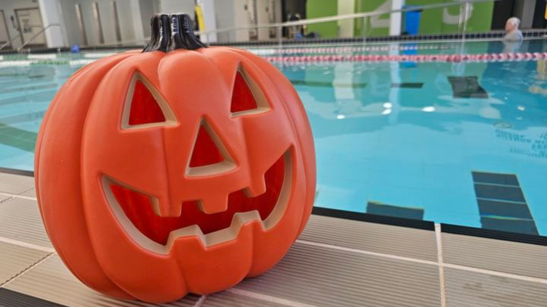 a halloween pumpkin sitting on the edge of a swimming pool