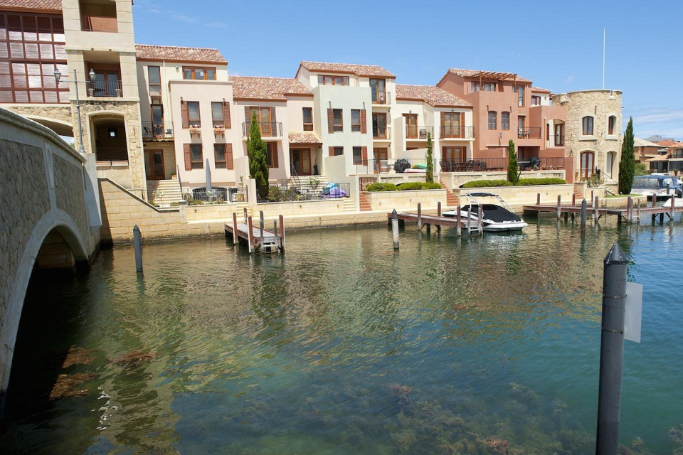 a marina with boats docked in front of a row of Italian-inspired houses