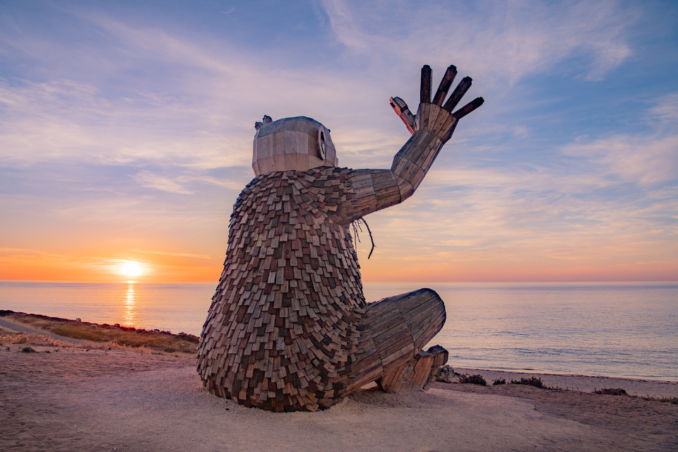 a wooden statue of a troll on the beach at sunset