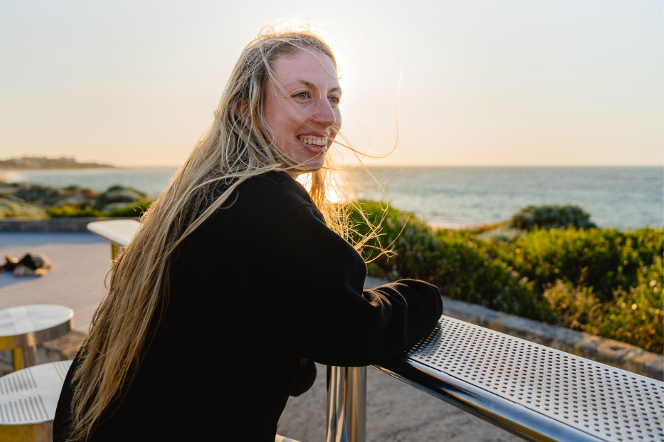 A woman with long blonde hair sitting on a bench overlooking the ocean